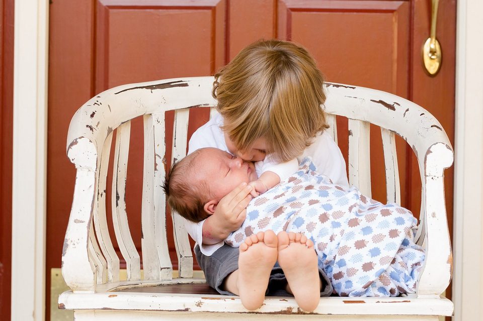 Foto van 'n dogtertjie wat op 'n bankie sit met 'n baba in haar arms